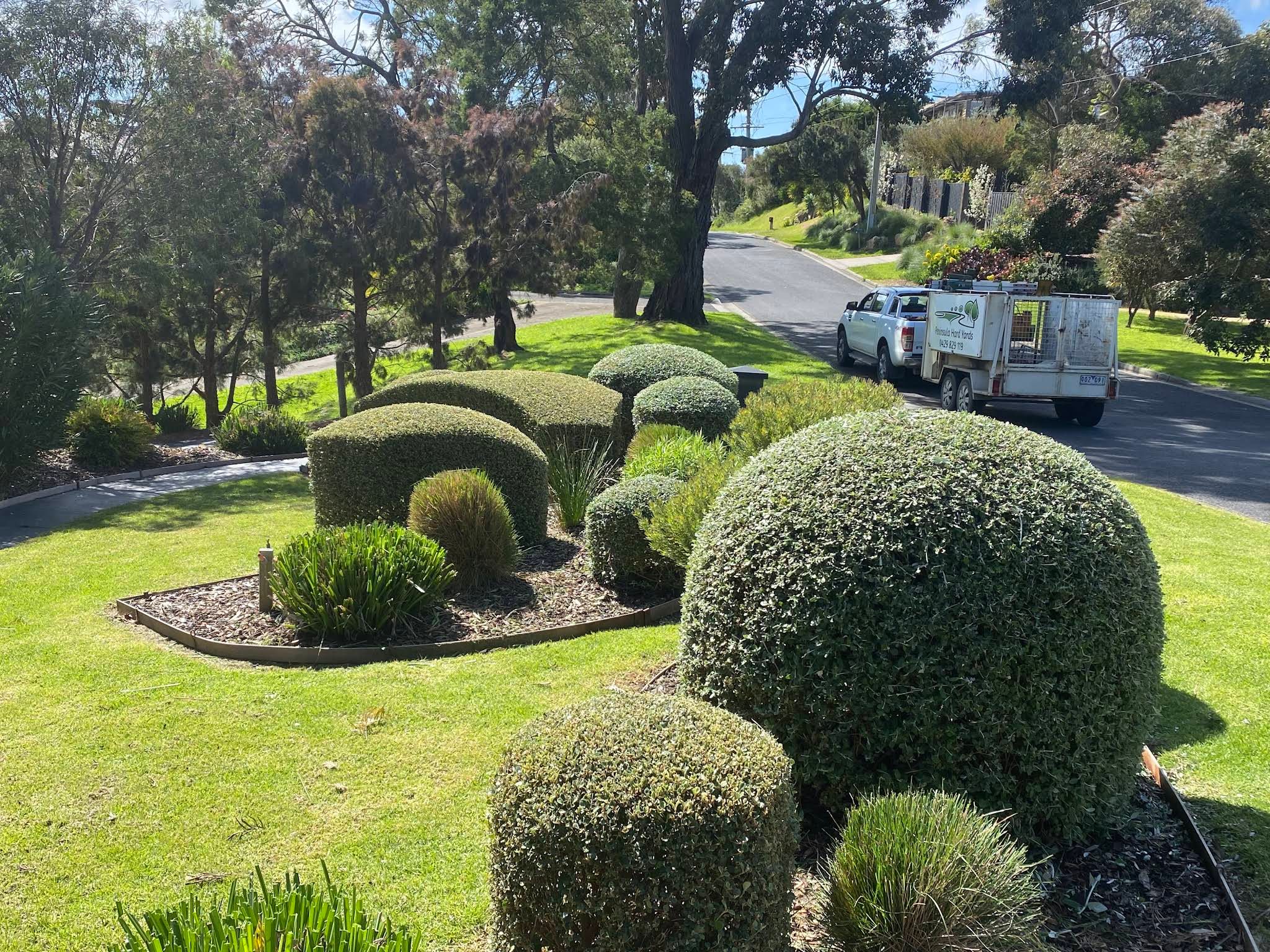 Rounded topiary and lawn with the Peninsula Hard Yards work vehicle nearby